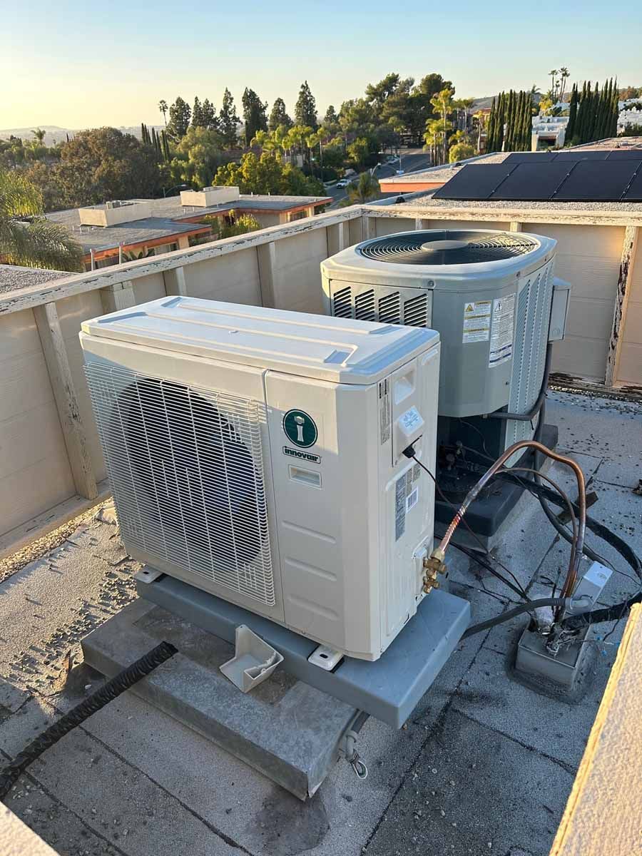 Rooftop HVAC equipment, including two outdoor AC units, beside a gravel roof edge at sunset.