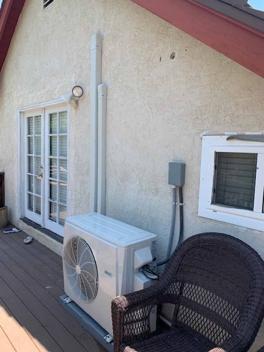 Patio wall with French doors, air conditioner, wicker chair, and deck railing