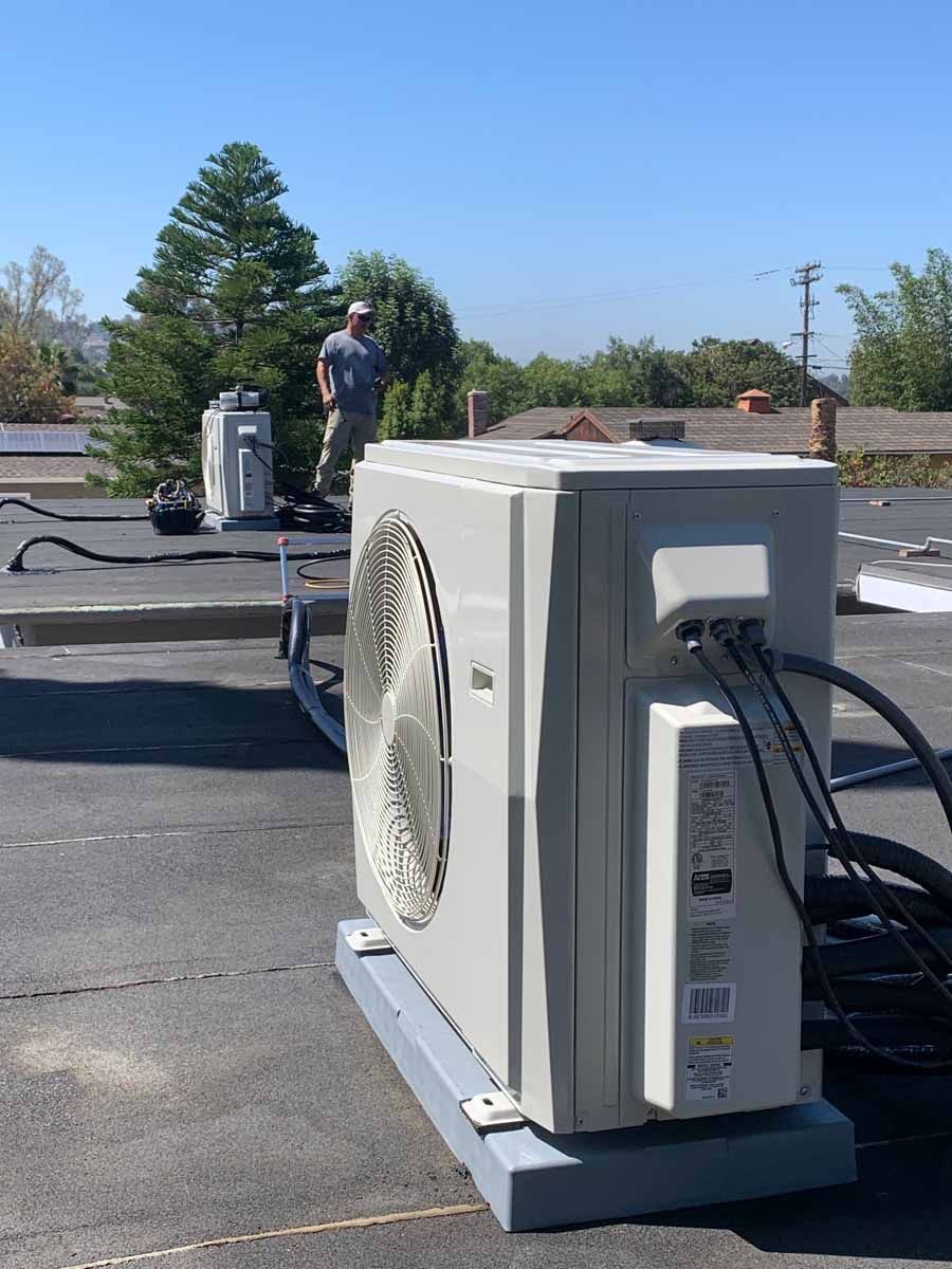 Outdoor rooftop HVAC condenser with hoses, and a worker standing in the background on a flat roof.