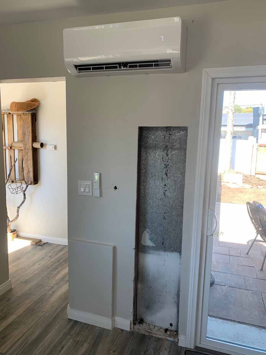 Interior room with wall-mounted air conditioner above a narrow doorway and a glass door on the right.