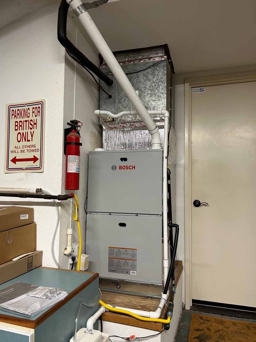 Utility room with a Bosch furnace, white vent pipes, red fire extinguisher, and beige door.
