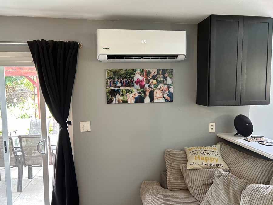 Cozy living room with gray walls, black curtains, wall-mounted AC, floral art, and a gray sofa.