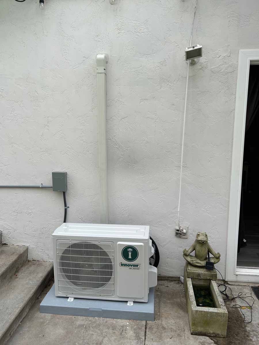Outdoor wall with a white air-conditioning unit, pipes, and a small utility basin beside steps.