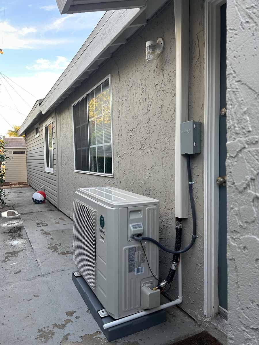 Gray stucco house side yard with a wall-mounted air conditioner and a window