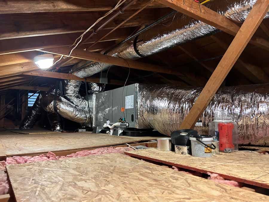 Attic with exposed wooden beams, insulation ducts, and loose flooring panels under construction