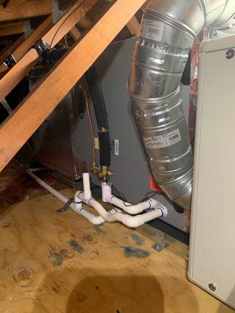 Attic HVAC area with white PVC pipes, silver ductwork, and wooden rafters over a water-stained floor
