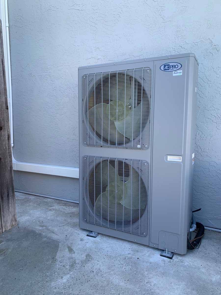 Gray outdoor HVAC unit against a wall on a concrete patio.