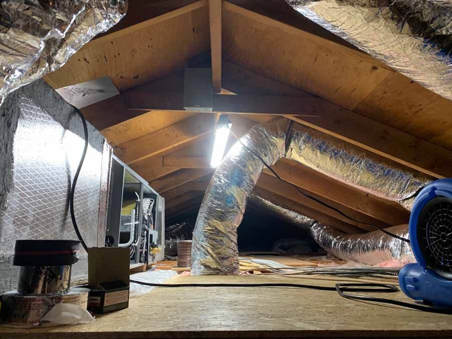 Attic with exposed beams, silver ductwork, and a blue blower fan on the floor