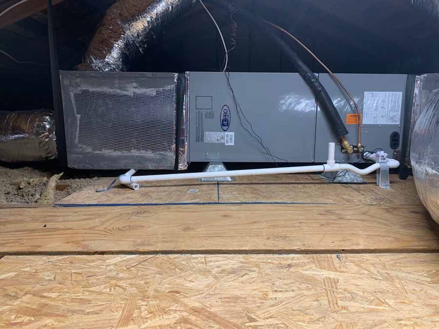 Attic HVAC unit with ducting, pipes, and wiring on a wooden floor under a sloped roof