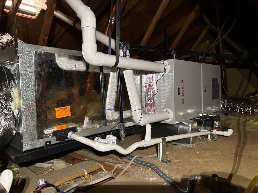 HVAC unit and ductwork in a cramped attic, with insulated pipes and wiring.