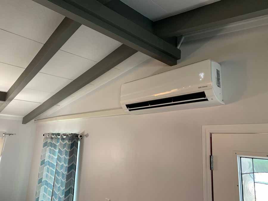 White wall-mounted air conditioner above a door in a room with exposed ceiling beams.