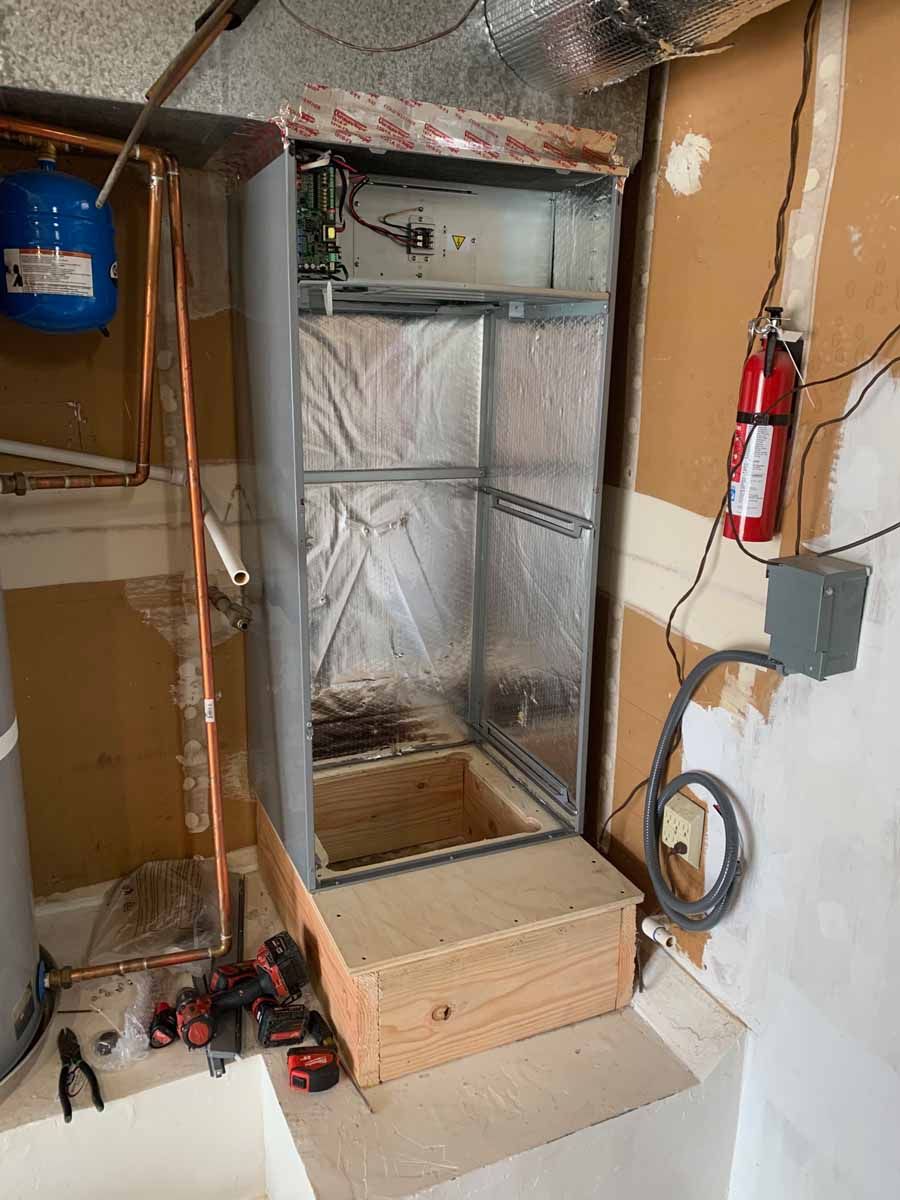 Open closet-style HVAC unit under construction, wrapped in plastic, with tools and a fire extinguisher nearby