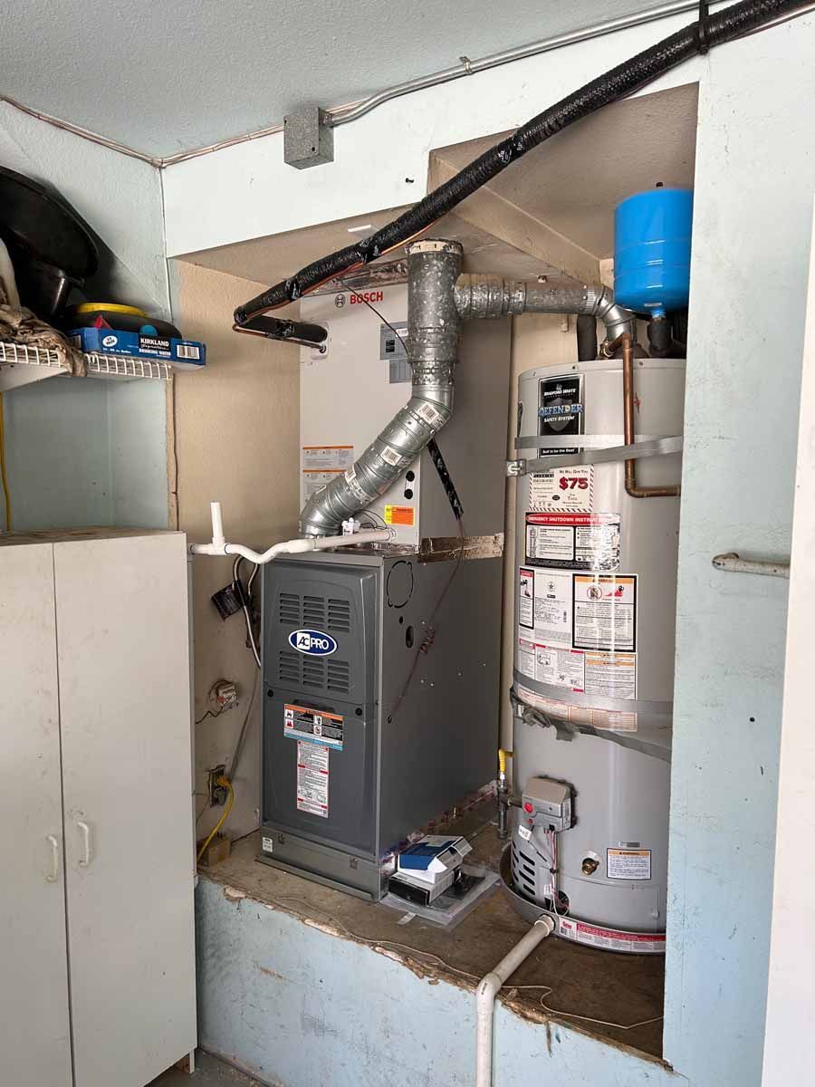 Basement utility room with furnace, water heater, and exposed silver ductwork beside a stairwell.