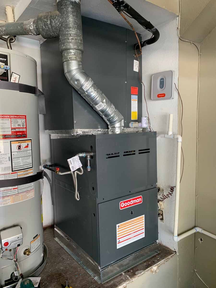 Gas furnace and water heater in a utility closet with silver ductwork and pipes.