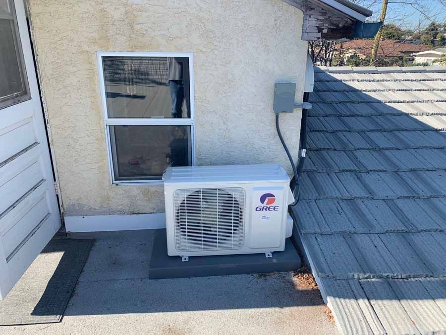 Outdoor air conditioner unit beside a stucco house wall and window on a rooftop deck