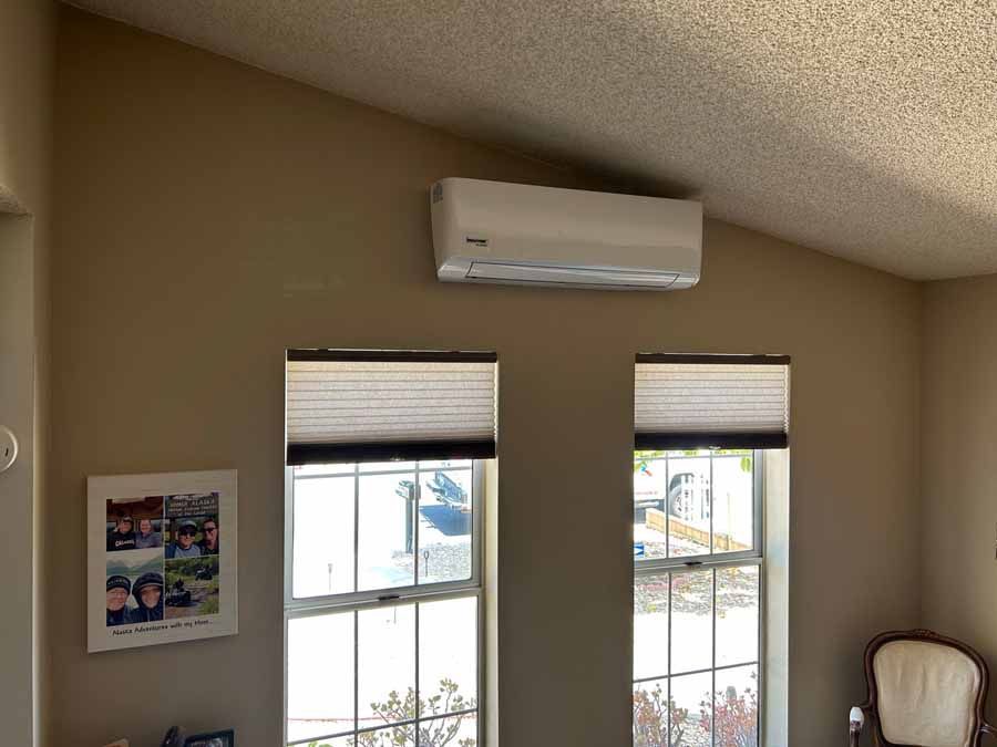 Living room wall with two windows, an air conditioner, framed art, and a chair