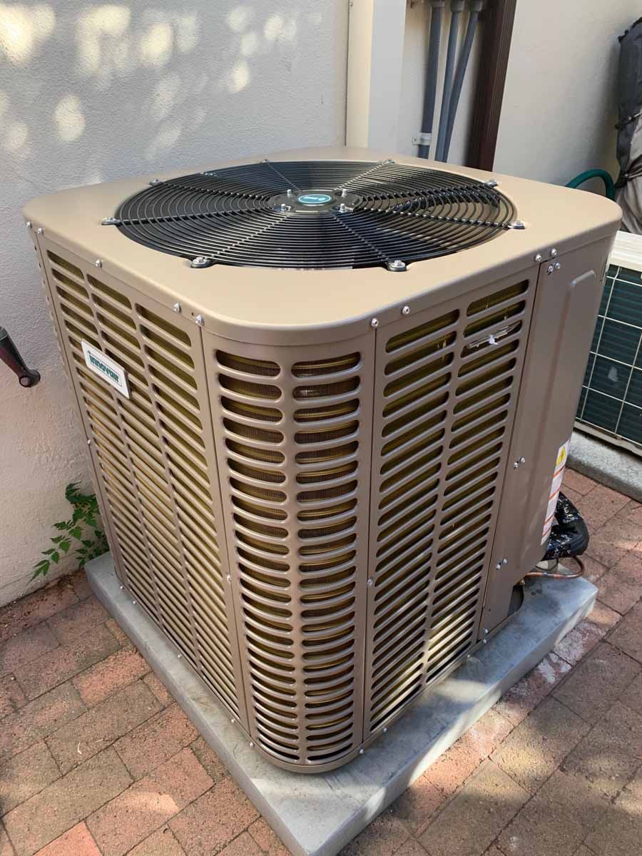 Outdoor central air conditioner unit beside a house wall, with beige vents and a black fan on top