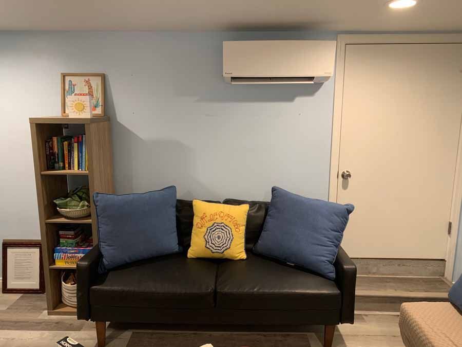 Living room with a black sofa, blue and yellow pillows, a bookshelf, wall AC, and a white door