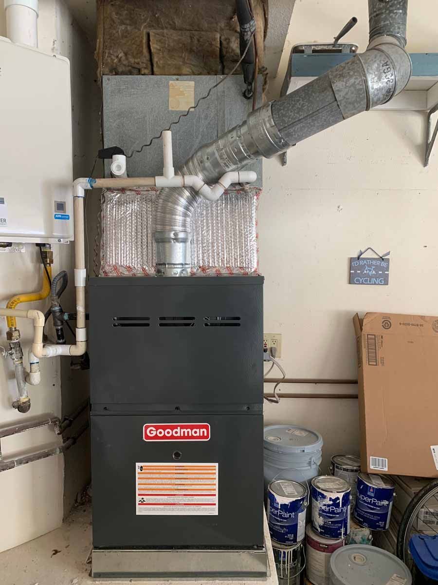 Gas furnace in a basement utility room with insulated ductwork, pipes, and paint cans nearby.