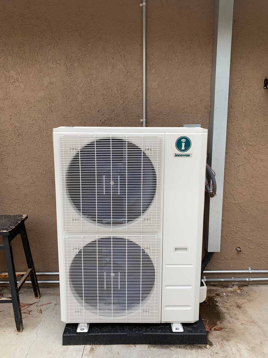 Outdoor air conditioning unit with two large fans against a brown wall