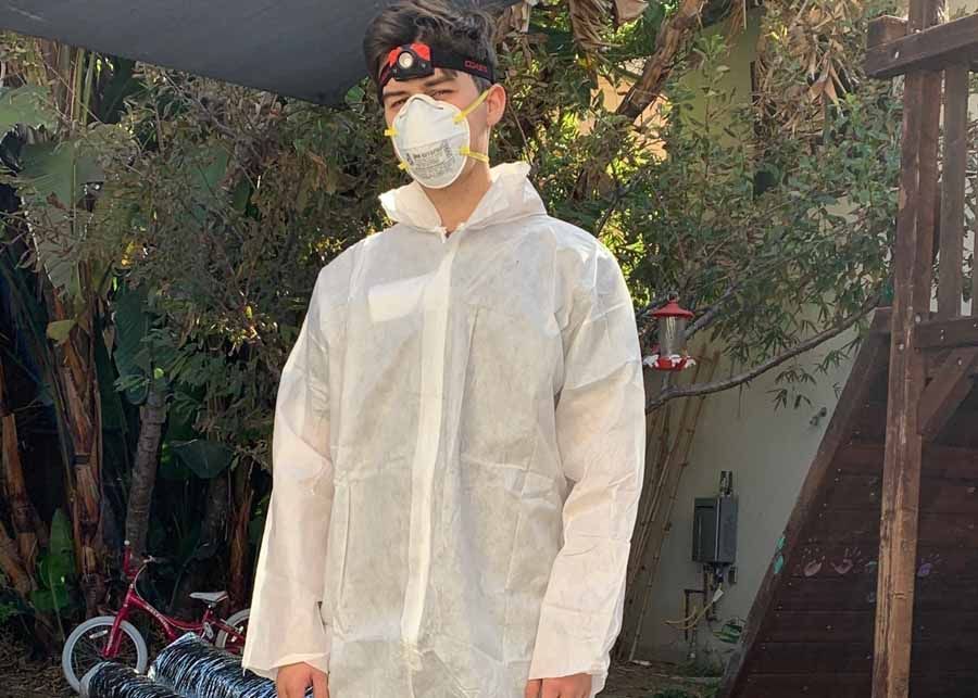 Person in a white protective suit and mask standing outdoors under a canopy.