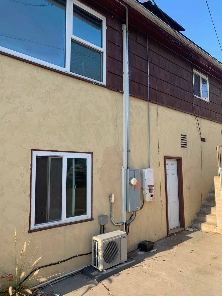 Exterior of a beige building with a window, utility pipes, electrical boxes, and an outdoor air conditioner unit.