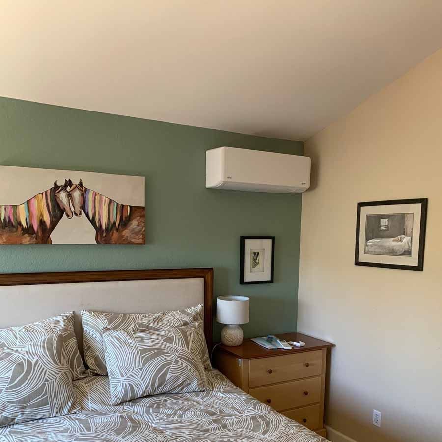 Cozy bedroom with patterned pillows, green accent wall, wood dresser, and wall-mounted air conditioner