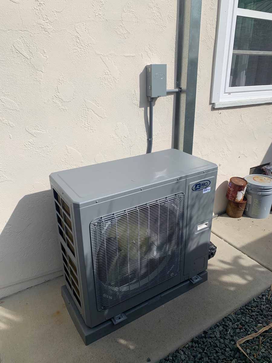 Outdoor HVAC unit beside a beige house wall, with vented fan grille and electrical box above.
