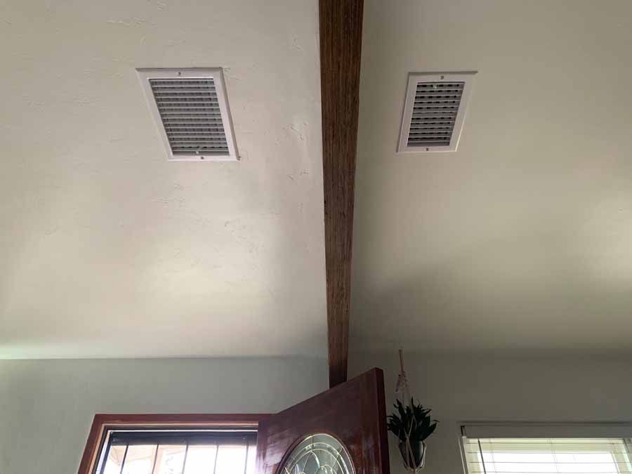 Ceiling with two air vents and a wooden beam above an open doorway