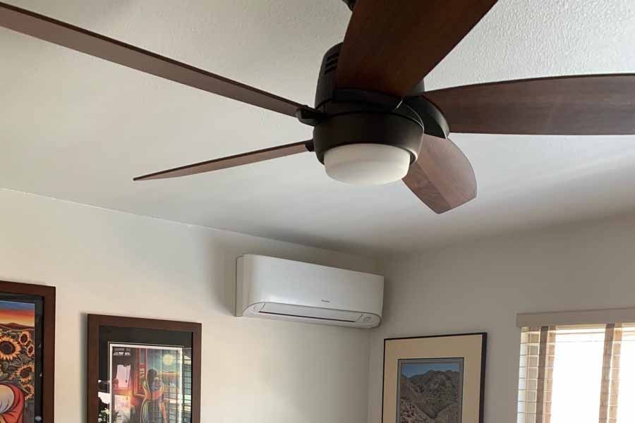 Ceiling fan and wall-mounted air conditioner in a bright room with framed artwork and window blinds