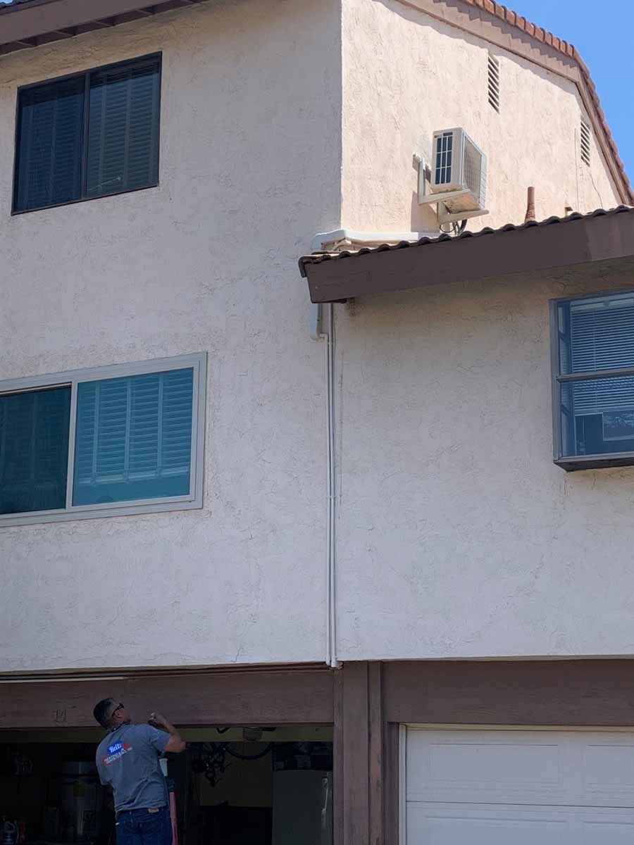 Man working under a white stucco house with blue shutters and a garage door