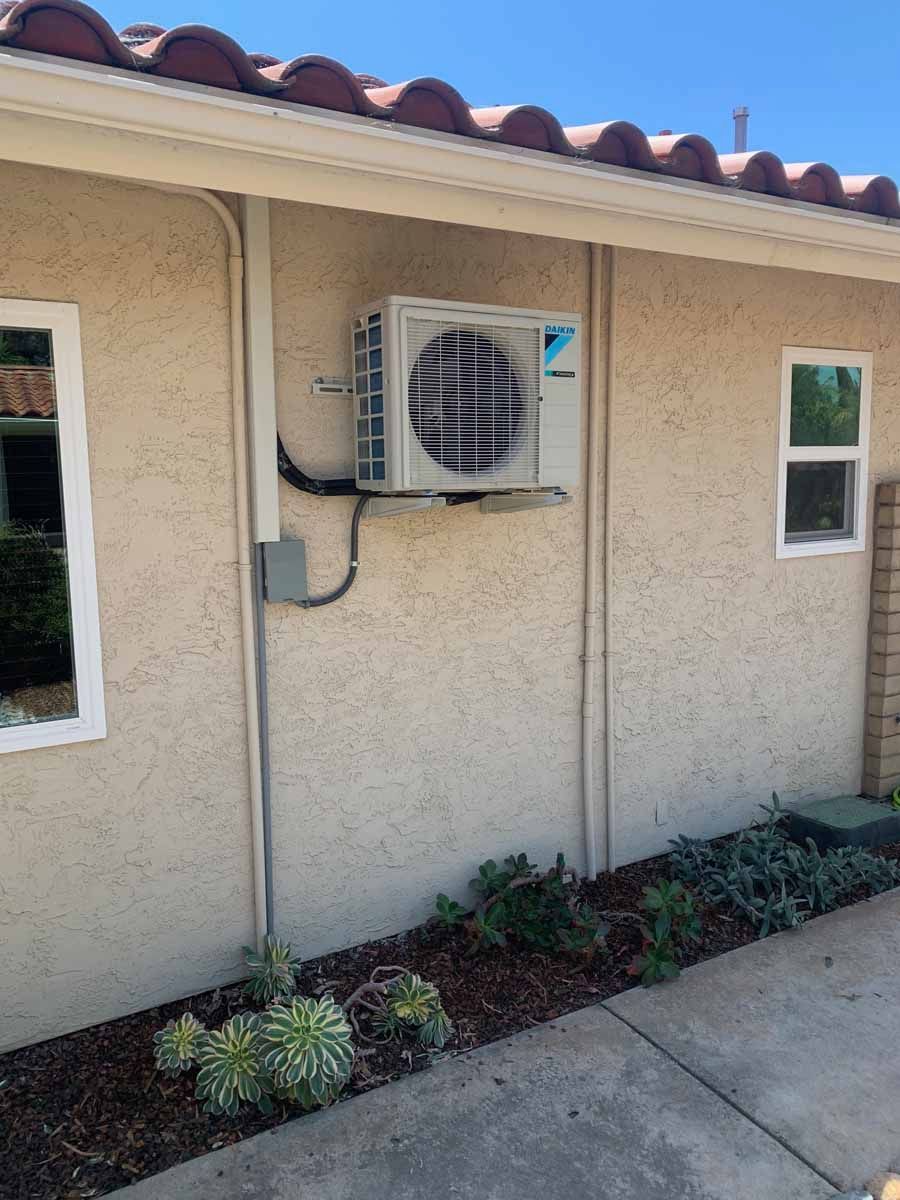 Exterior wall with a mounted air conditioning unit and two small windows above a concrete walkway
