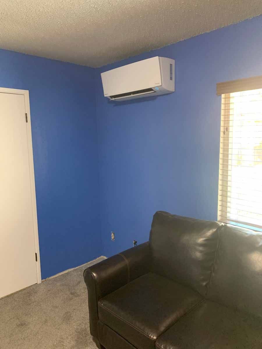 Small room with blue walls, a wall-mounted AC, window blinds, closet door, and a black leather chair.