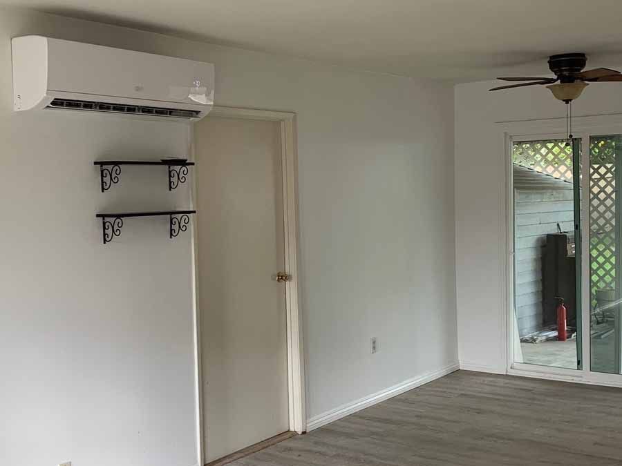 Empty living room with wall-mounted air conditioner, shelves, and sliding glass doors.