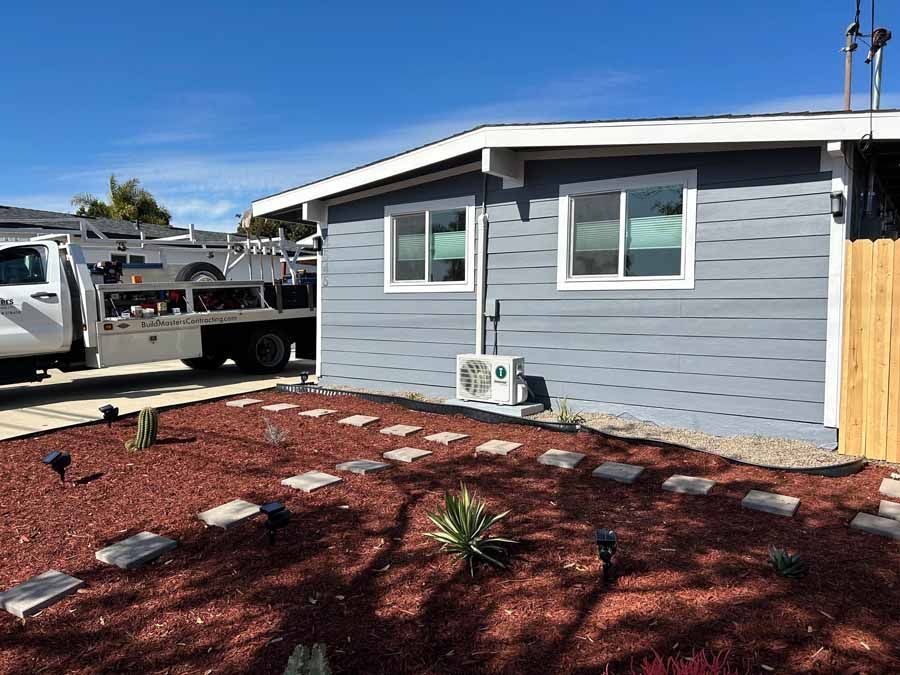 Gray house exterior with white trim, a parked truck, and a red gravel front yard with stepping stones.