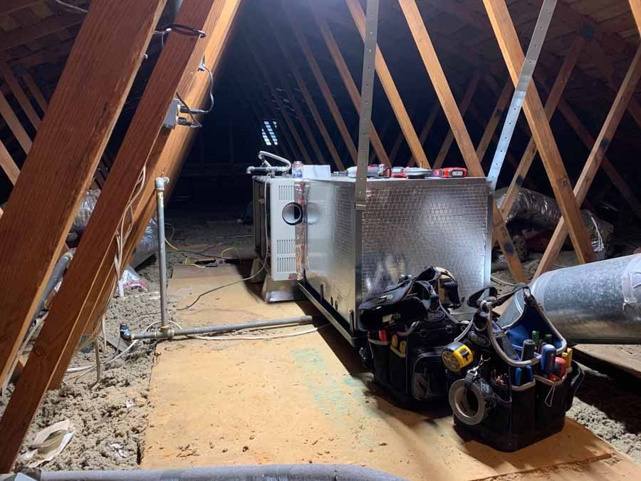 Attic with exposed rafters, HVAC equipment, and tools on a wooden floor.