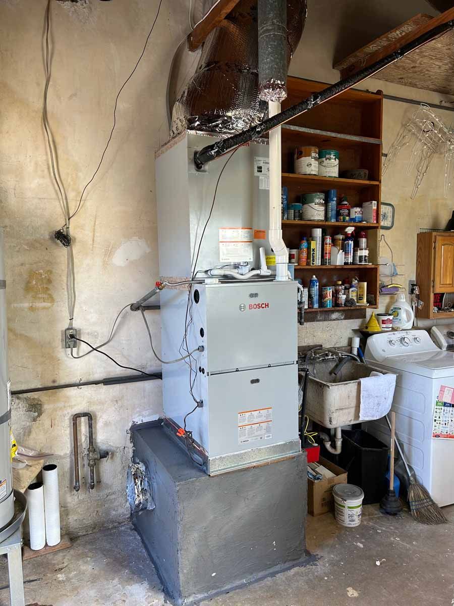 Utility room with a gas furnace and exposed ductwork beside shelves of supplies