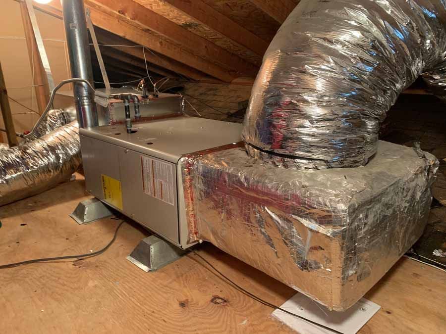 Attic HVAC unit with silver ductwork and insulated vents on a wooden floor