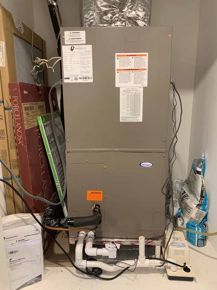 Gray HVAC furnace in a utility closet with exposed pipes, wiring, and ductwork.