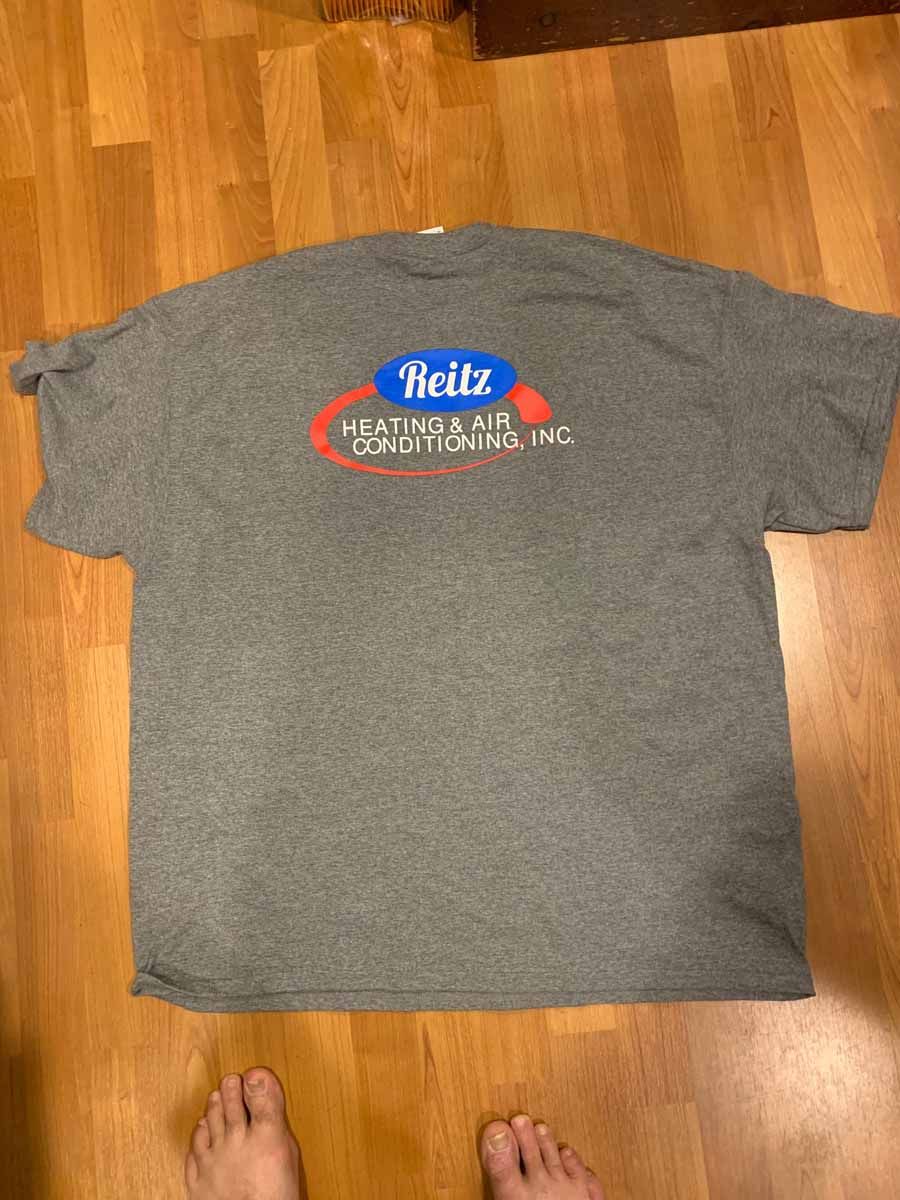 Gray Reitz T-shirt laid flat on a wooden floor with a visible logo on the chest