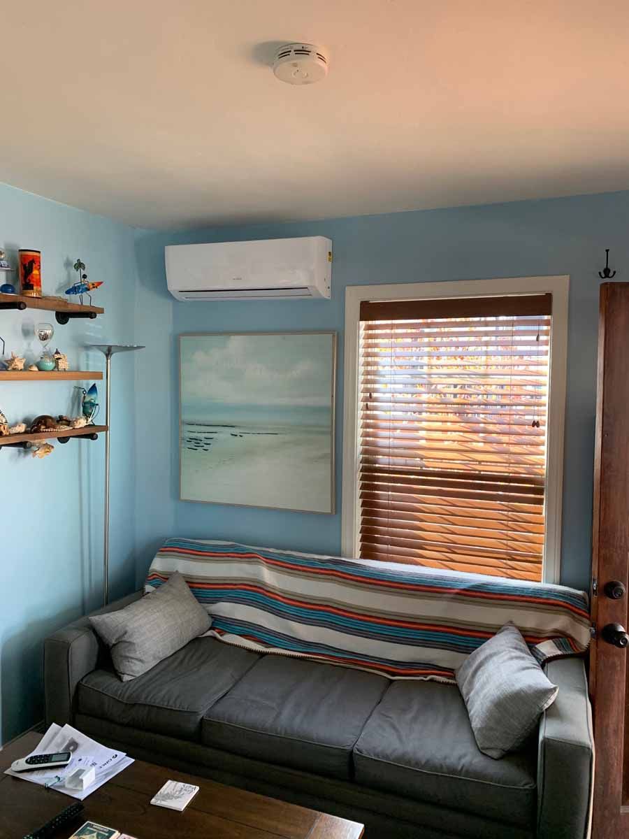Blue living room with gray couch, beach painting, wall shelves, and window blinds filtering sunlight