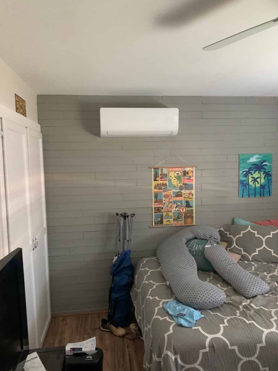 Small bedroom with a bed, wall art, gray patterned bedding, and a wall-mounted air conditioner.