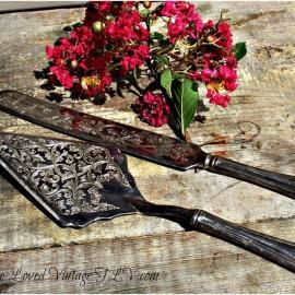 Victorian-style engraved knife and fork beside a bouquet of red flowers on rustic wood.