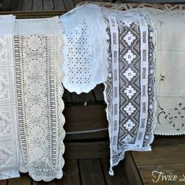 White and cream lace table runners and doilies hanging over a wooden bench outdoors