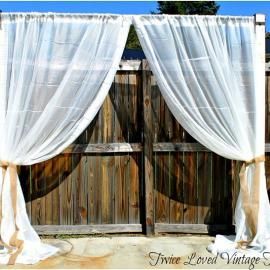 White sheer curtains draped over rustic wooden double doors against a blue sky