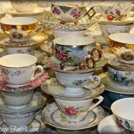 Stacked floral teacups and saucers in a tea set display, mostly white with pink and gold accents