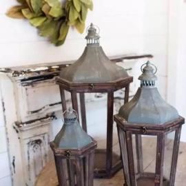 Three rustic metal lanterns with glass panels on a white shelf