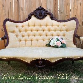 Cream tufted vintage loveseat with dark carved wood trim and a small pink flower bouquet on the seat.