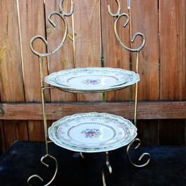 Two-tier metal plate stand with floral plates against a wooden fence
