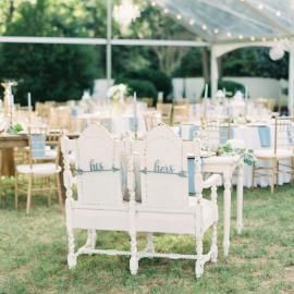 White vintage-style chairs and round tables set under a tent for an outdoor event